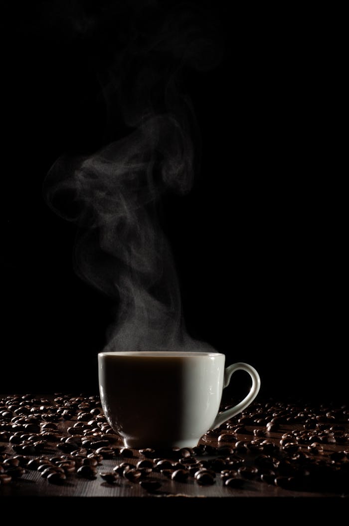 A steaming cup of coffee surrounded by beans on a dark background, creating a warm, inviting mood.